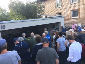 Eine Menschenmenge steht vor einer Garage, Peter Ritter erklärt die Funktionsweise eines Balkonkraftwerks. Auf dem Dach der Garage zwei Solarmodule.