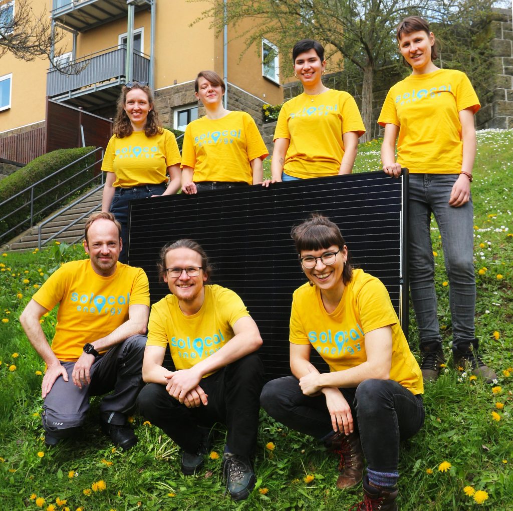 Teamfoto der sieben Kollektivmitglieder von SoLocal Energy mit gelben T-Shirts und Photovoltaik-Modul