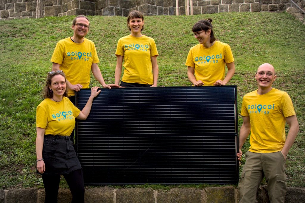 Teamfoto SoLocal Energy von März 2024: Anni, Arvid, Anne, Kerstin und Lukas stehen in ihren gelben SoLocal Energy-Shirts rund um ein PV-Modul