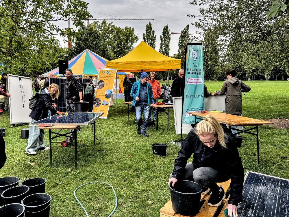 Menschen, die gebrauchte Photovoltaik-Module putzen und deren Stecker tauschen in einem Park mit gelbem Pavillon.