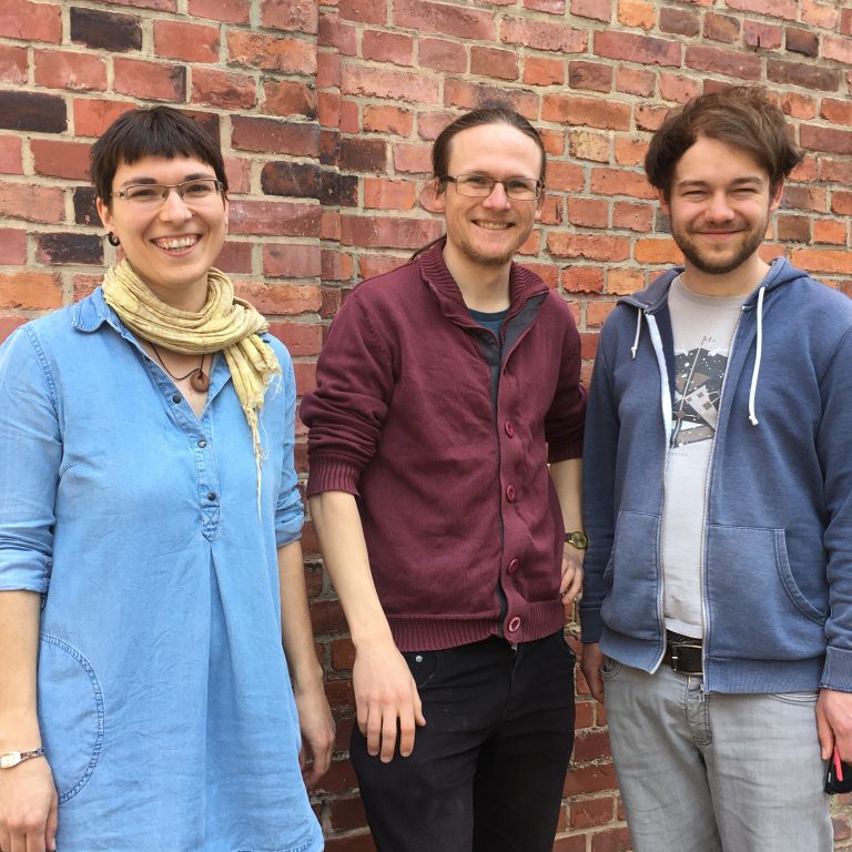 Kerstin Lopau, Arvid Jasper und Benedikt Breuer vor einer Backsteinmauer